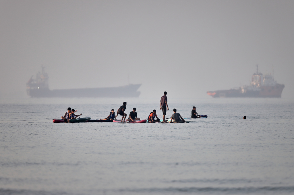 People gather on paddleboards in shallow water as cargo and service vessels are anchored in the Strait of Hormuz off Bandar Abbas, Iran, Monday, June 1, 2026. (Amirhosein Khorgooi/ISNA via AP)