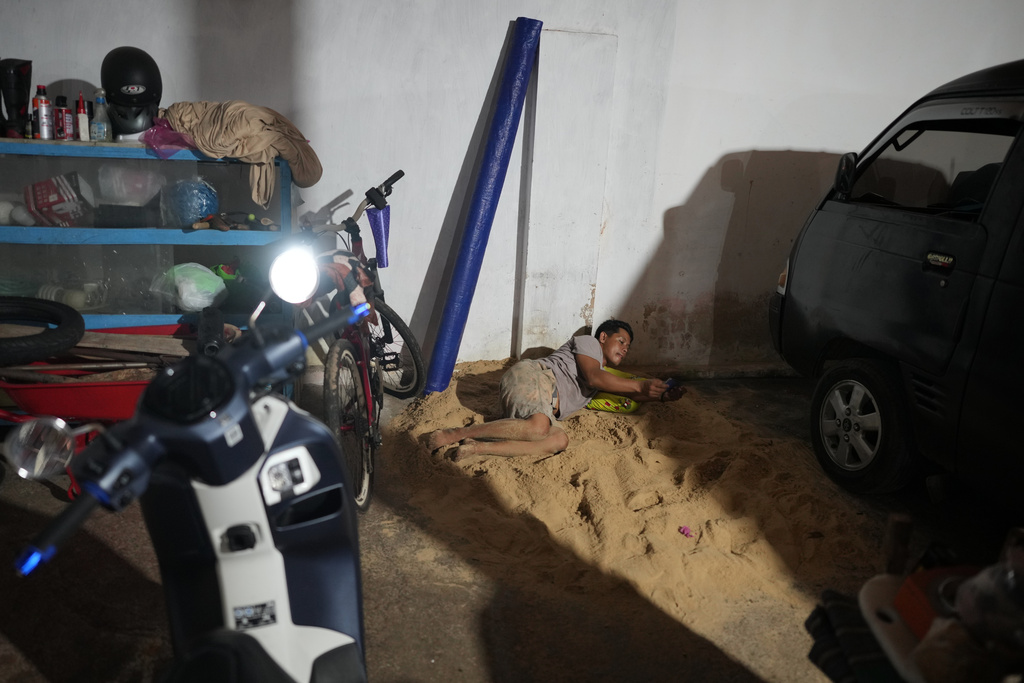 Iskandar checks his mobile phone as he lies on sand in Legung Timur village in Sumenep on Madura Island, Indonesia, Tuesday, Sept. 9, 2025. (AP Photo/Dita Alangkara)