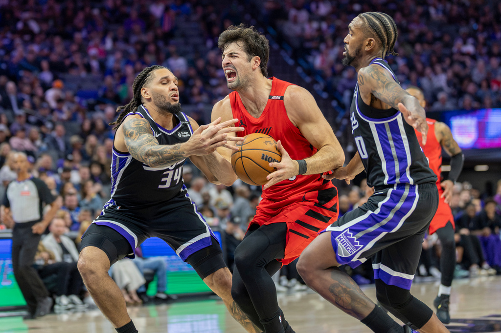 Portland Trail Blazers forward Deni Avdija, center, drives to the basket with Sacramento Kings guards Emanuel Sharp (34) and Malik Monk (0) defending during the first half of an NBA basketball game Friday, Oct. 23, 2026, in Sacramento, Calif. (AP Photo/Sara Nevis)