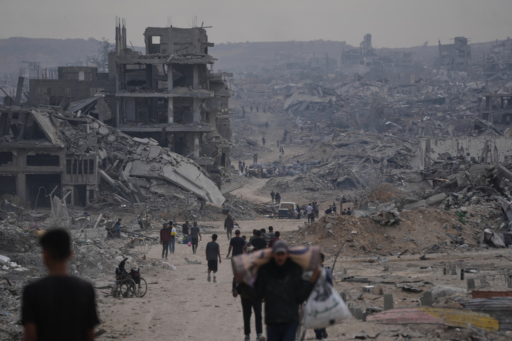 Displaced Palestinians walk with their belongings along the heavily damaged Al-Jalaa Street in Gaza City, Sunday, Oct. 12, 2025, after Israel and Hamas agreed to a pause in their war and the release of the remaining hostages. (AP Photo/Abdel Kareem Hana)