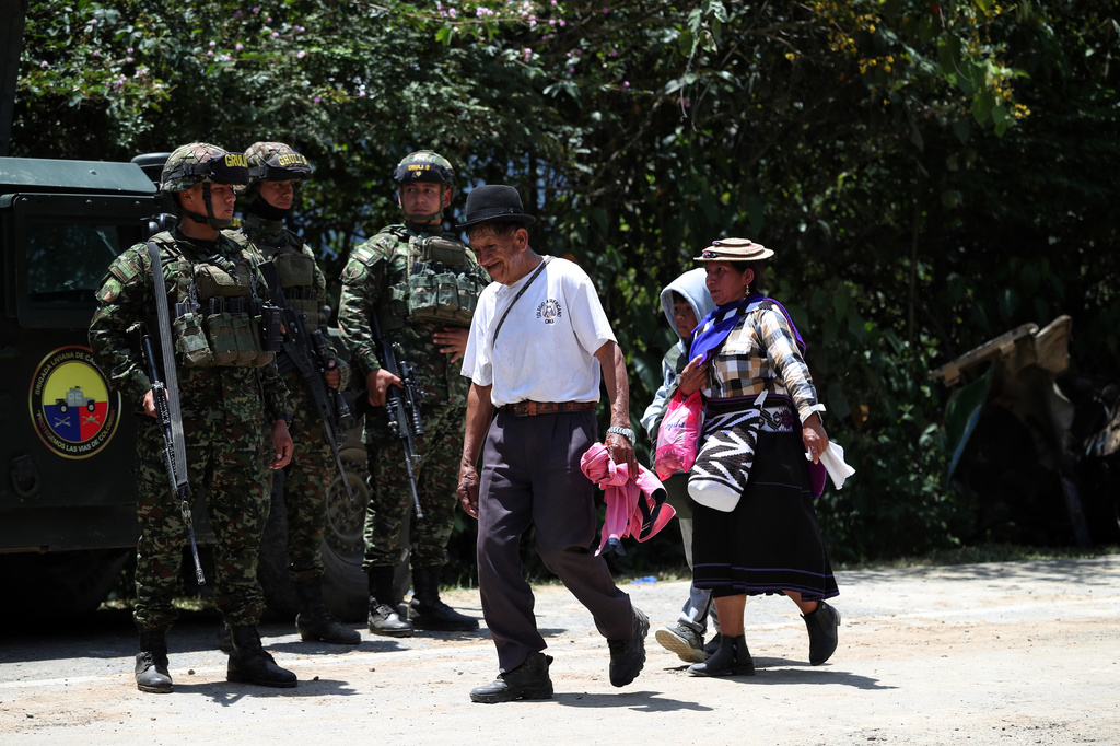 People walk past soldiers guarding at the site of the attack on the Pan-American Highway in Cajibio, Colombia, Sunday, April 26, 2026, a day after an assault that killed at least 20 people and that authorities blamed on dissident groups of the former FARC rebels. (AP Photo/Santiago Saldarriaga)