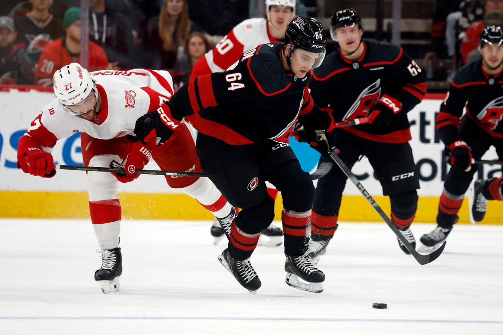Carolina Hurricanes' Joel Nystrom (64) tries to control the puck with Detroit Red Wings' Michael Rasmussen (27) nearby during the first period of an NHL hockey game in Raleigh, N.C., Saturday, Dec. 27, 2025. (AP Photo/Karl DeBlaker)