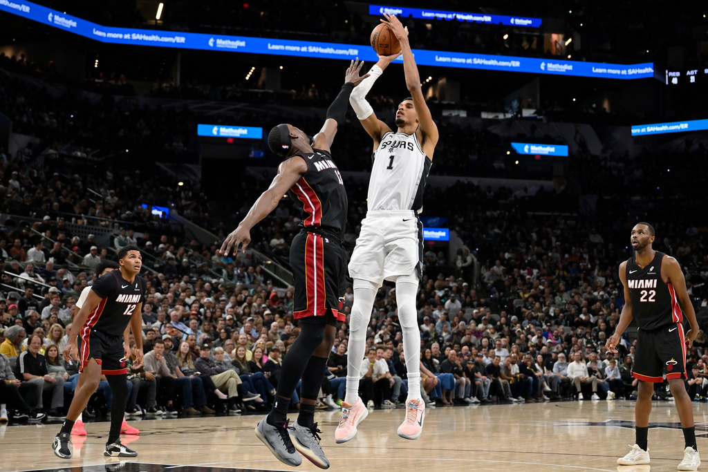 San Antonio Spurs center Victor Wembanyama (1) goes up to shoot against Miami Heat forward Bam Adebayo, center left, during the second half of an NBA basketball game, Thursday, Oct. 30, 2025, in San Antonio. (AP Photo/Darren Abate)