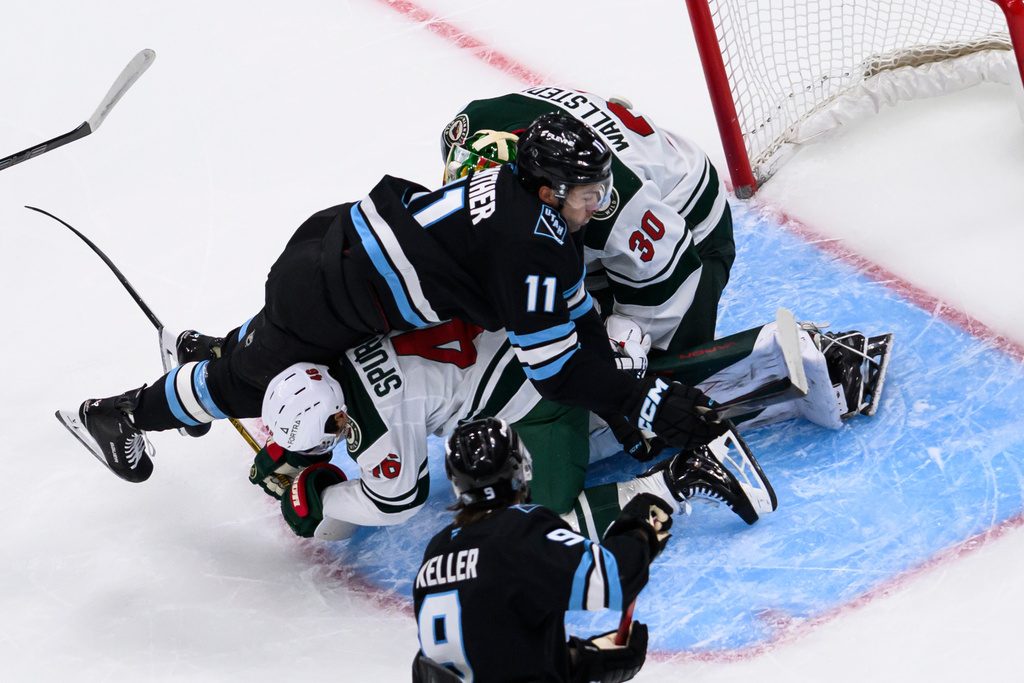 Utah Mammoth right wing Dylan Guenther (11) is knocked down in front of the net by Minnesota Wild defenseman Jared Spurgeon, bottom center, during the first period of an NHL hockey game, Friday, Feb. 27, 2026, in Salt Lake City. (AP Photo/Tyler Tate)