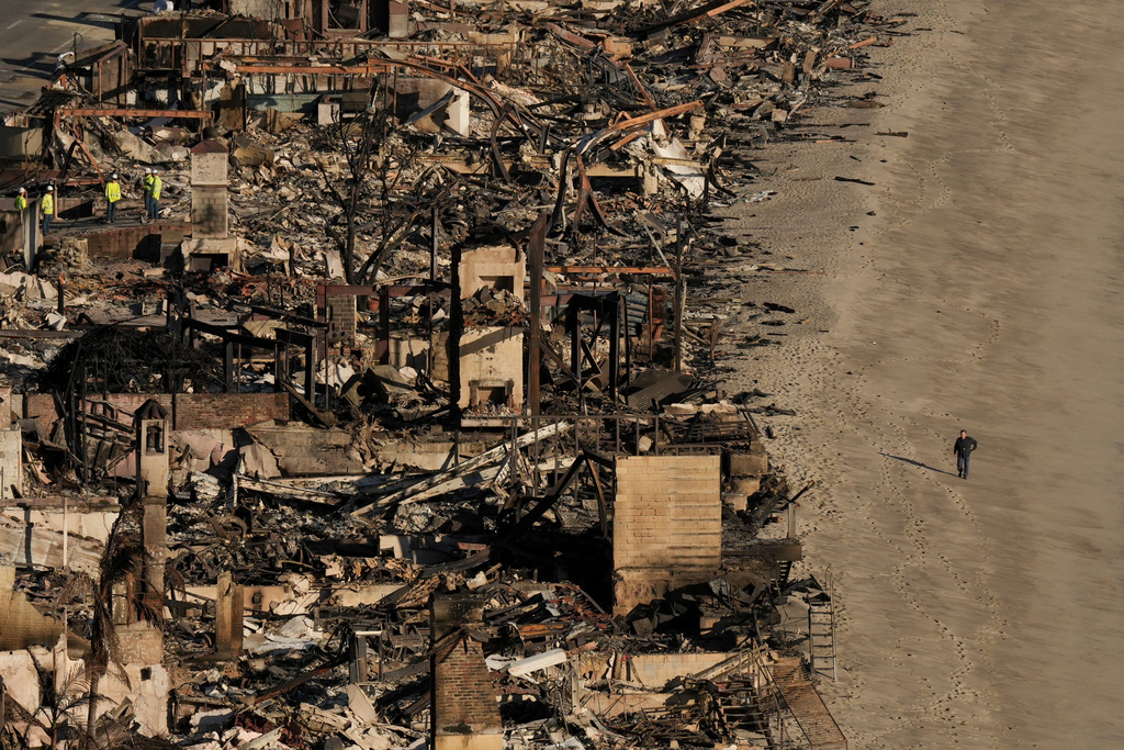 FILE - A person walks on the beach next to homes damaged by the Palisades Fire, Jan. 16, 2025 in Malibu, Calif. (AP Photo/Jae C. Hong, file)
