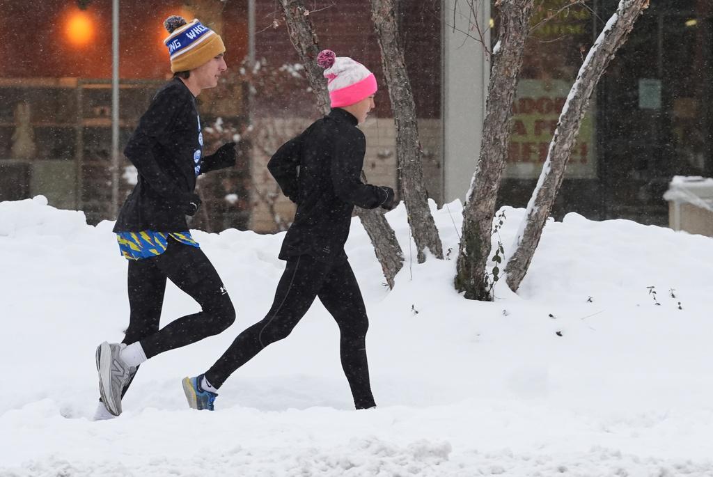 Pedestrians run on a snow-covered sidewalk during a snowy day in Wheeling, Ill., Monday, Dec. 1, 2025. (AP Photo/Nam Y. Huh)