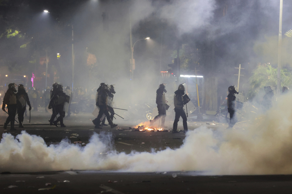 Police officers walk amid tear gas smoke during a protest in Surabaya, East Java, Indonesia, Saturday, Aug. 30, 2025, sparked by reports of lawmakers receiving excessive housing allowances. (AP Photo/Trisnadi)