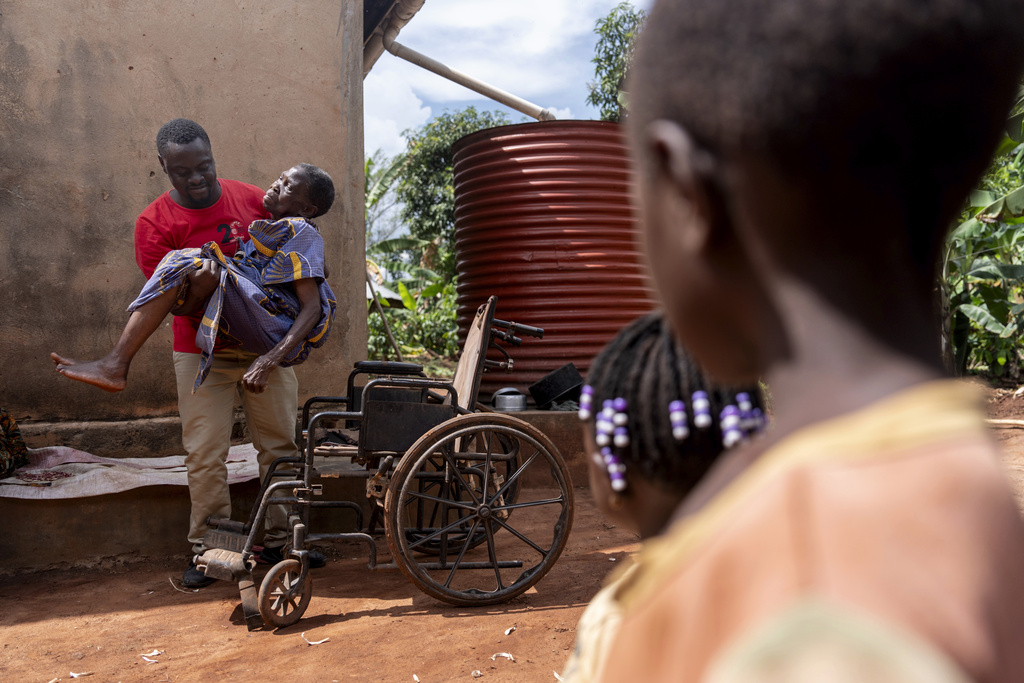 Field assistant Tyler Tukamuhabwa lifts Alice Janet Nakagwe, who is about 93, into a wheelchair to have her ears cleaned as part of a nurse's visit by the NGO Reach One Touch One Ministries in Magogo, Uganda, Saturday, Nov. 16, 2024. (AP Photo/David Goldman)