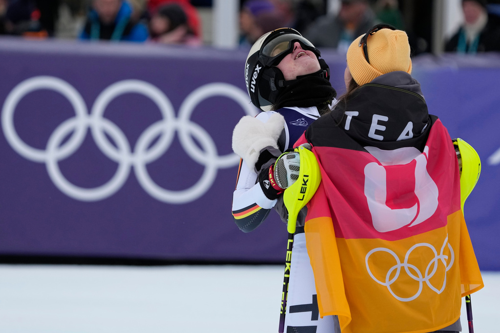 Germany's Emma Aicher, left, is hugged by teammate Germany's Kira Weidle Winkelmann at the finish area of an alpine ski, women's team combined race, at the 2026 Winter Olympics, in Cortina d'Ampezzo, Italy, Tuesday, Feb. 10, 2026. (AP Photo/Andy Wong)