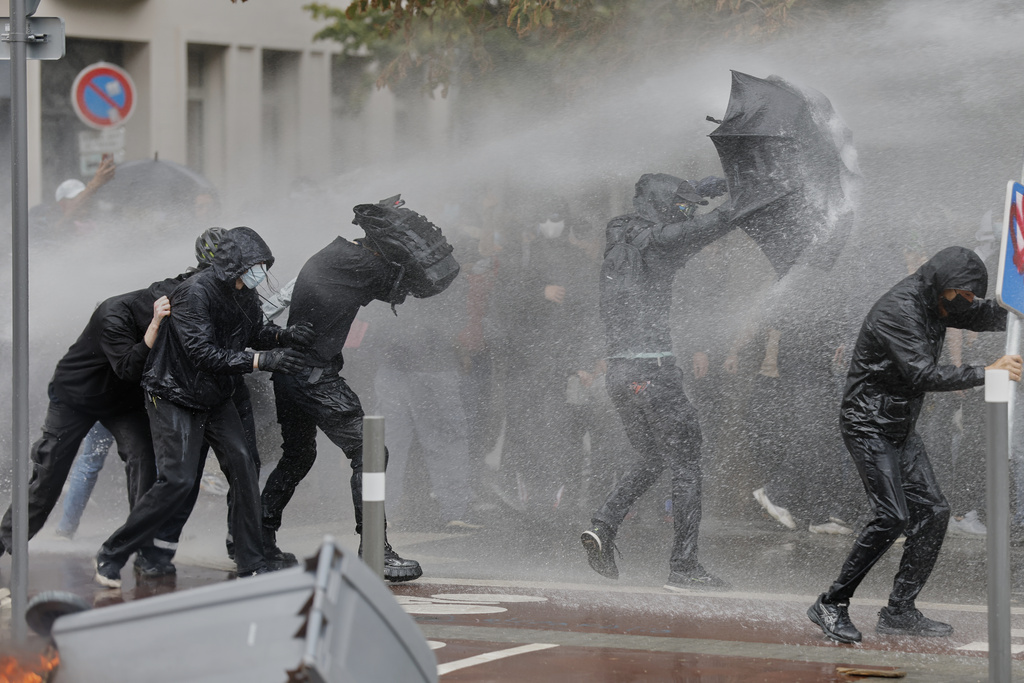 A protesters of the "Block Everything" movement takes cover of a water canon behind an umbrella in Lille, northern France, Wednesday, Sept. 10, 2025. (AP Photo/Jean-Francois Badias)