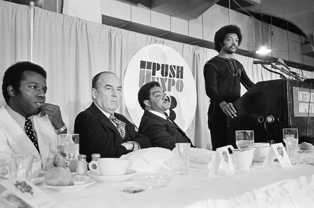 Rev. Jesse Jackson speaks at the PUSH Expo businessmen's breakfast as, from left, Richard G. Hatcher, mayor of Gary, Ind., Emmitt Dedmon, and George E. Johnson Sr., listen, in Chicago, Sept. 19, 1973. (Chicago Sun-Times via AP)
