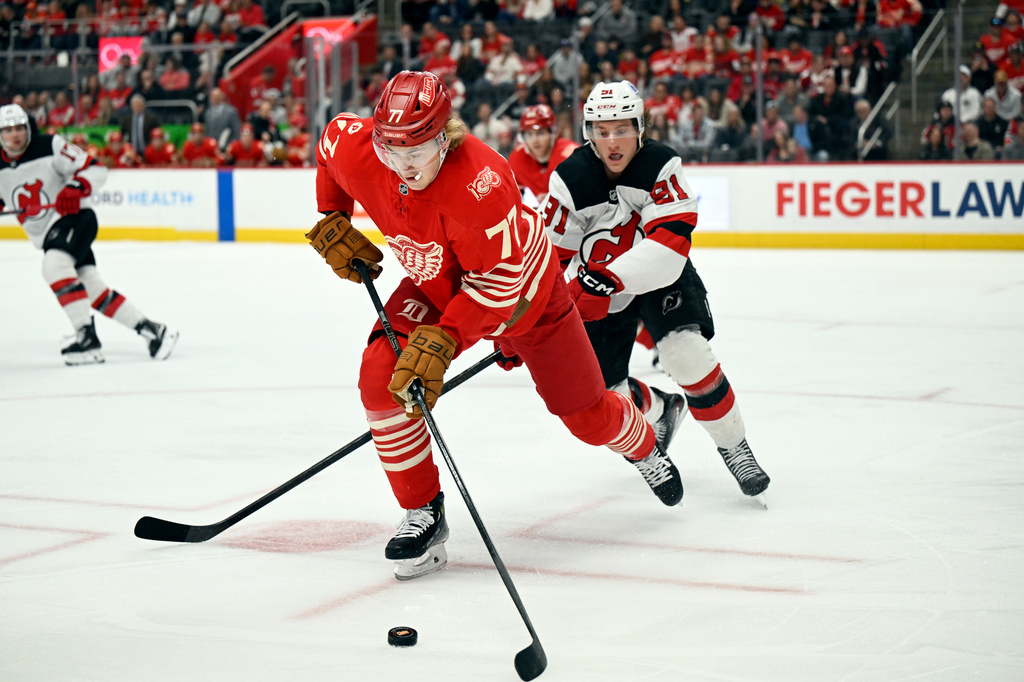 Detroit Red Wings defenseman Simon Edvinsson (77) moves the puck away from New Jersey Devils center Dawson Mercer, back right, during the first period of an NHL hockey game, Saturday, April 11, 2026, in Detroit. (AP Photo/Jose Juarez)