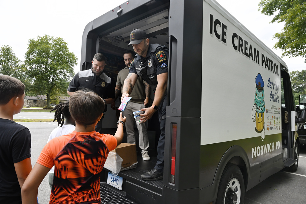 Norwich Police School Resource Officer Bob McKinney hands an ice cream to children finishing a summer camp activity in Norwich, Conn., on Thursday, Aug. 21, 2025. (AP Photo/Jessica Hill)
