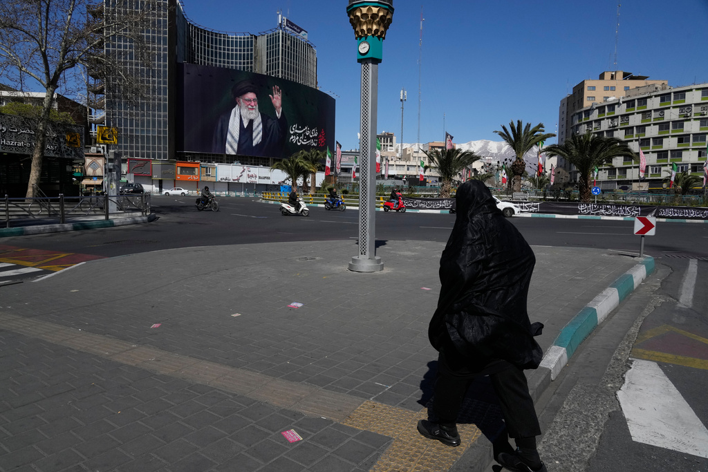 A woman crosses almost deserted square with a billboard at rear showing a portrait of the late Iranian Supreme Leader Ayatollah Ali Khamenei, who was killed in the U.S.–Israeli military campaign, in Tehran, Iran, Tuesday, March 3, 2026. (AP Photo/Vahid Salemi)