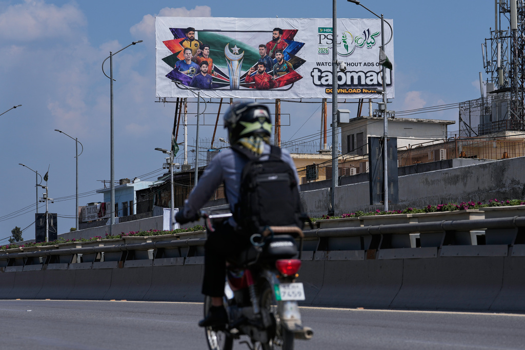 A motorcyclist drives past a billboard of Pakistan's premier domestic T20 the Pakistan Super League, which will take place in empty stadiums due to the recent spike in oil prices, in Rawalpindi, Pakistan, Tuesday, March 24, 2026. (AP Photo/Anjum Naveed)