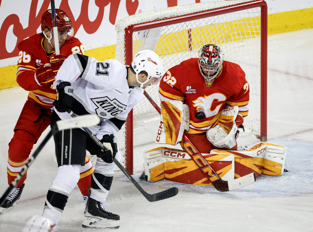 Los Angeles Kings' Scott Laughton, centre, has his shot blocked by Calgary Flames goalie Dustin Wolf, right, as Zach Whitecloud checks during the second period of an NHL hockey game in Calgary on Tuesday, March 24, 2026. (Jeff McIntosh/The Canadian Press via AP)
