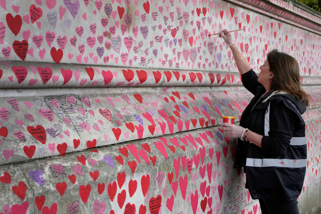 FILE - Volunteer Fran Hall, who lost her husband Steve Mead to COVID-19, re-paints faded hearts on the COVID-19 memorial wall in Westminster in London, Friday, Oct. 15, 2021. (AP Photo/Kirsty Wigglesworth, File)