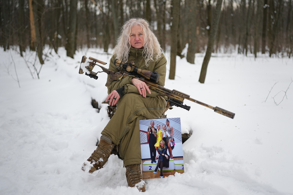 Tetiana Khimion 47, now a sniper in the Ukrainian army, poses with a photograph of herself as a dance teacher taken before Russia's full-scale invasion, in a park in Kyiv, Ukraine, Sunday, Feb. 22, 2026. (AP Photo/Sergei Grits)