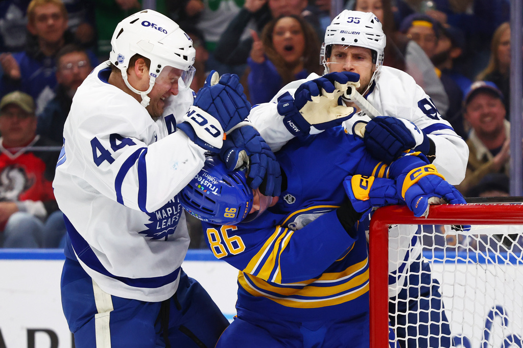 Buffalo Sabres center Noah Ostlund (86) is grabbed by Toronto Maple Leafs defenseman Morgan Rielly (44) and defenseman Oliver Ekman-Larsson (95) during the first period of an NHL hockey game Saturday, March 14, 2026, in Buffalo, N.Y. (AP Photo/Jeffrey T. Barnes)