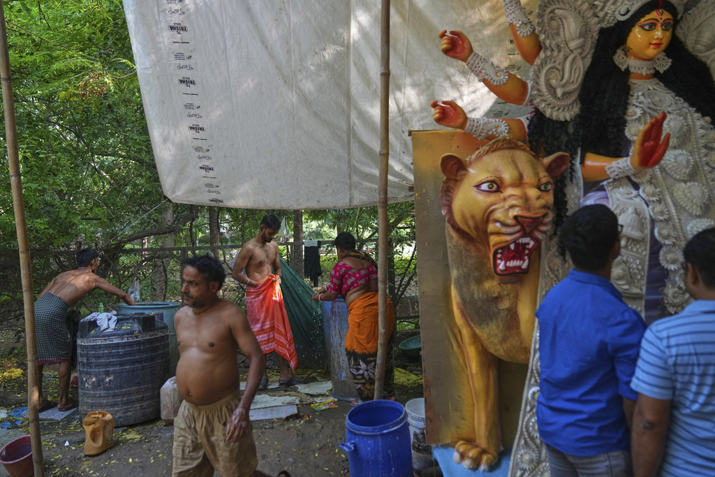 Workers and artists bathe while visitors look at an idol of the Hindu goddess Durga, which was created ahead of the Durga Puja festival in New Delhi, India, Saturday, Sept. 20, 2025. (AP Photo/Manish Swarup)