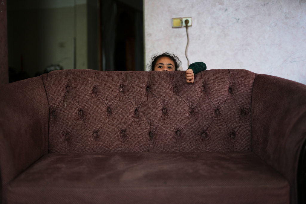 Habiba al-Kafarna, 5, who was orphaned when her parents, Ahmed and Sajida, were killed in an Israeli strike on a school sheltering displaced people in 2025, stands behind a sofa in the Gaza City home where she lives, May 31, 2026. (AP Photo/Abdel Kareem Hana)