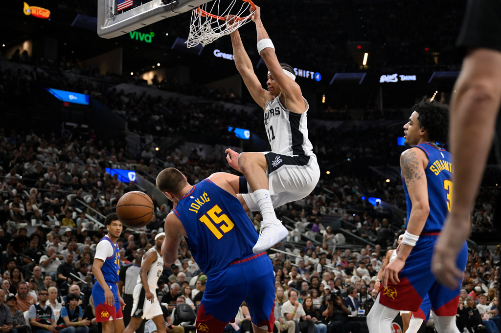 San Antonio Spurs forward Carter Bryant (11) dunks over Denver Nuggets center Nikola Jokic during the first half of an NBA basketball game, Sunday, April 12, 2026, in San Antonio. (AP Photo/Darren Abate)