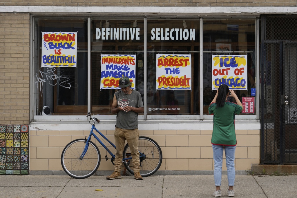 People stop to take pictures of signs posted on windows at a clothing store during the 2025 Pilsen Mexican Independence Day parade Saturday, Sept. 6, 2025, in Chicago. (AP Photo/Carolyn Kaster)