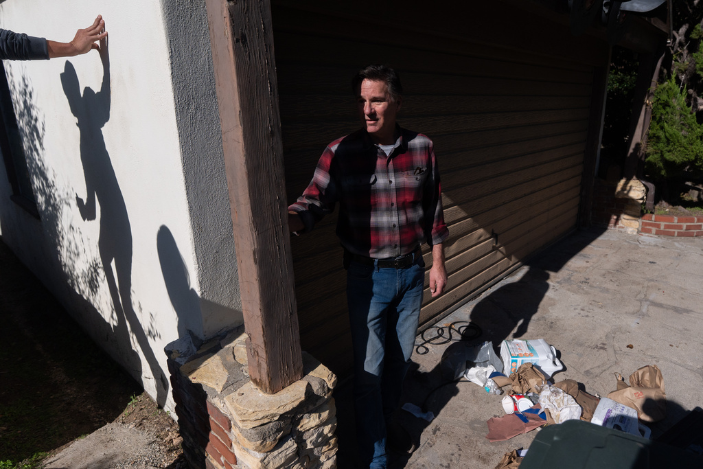 Homeowner Ken Johnson stands outside his house with trash scattered across the driveway after a bear took refuge in a crawl space at his property in Altadena, Calif., Monday, Dec. 1, 2025, as a reporter surveying the scene casts a shadow on a wall. (AP Photo/Jae C. Hong)