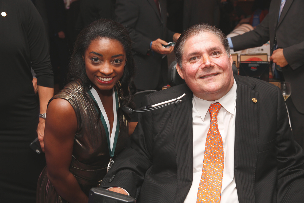 In this photo released by The Buoniconti Fund to Cure Paralysis, Olympic gold medal winning gymnast Simone Biles, left, poses with The Buoniconti Fund to Cure Paralysis President Marc Buoniconti at the 2018 Great Sports Legends Dinner, Sept. 24, 2018, to benefit the fund in New York. (The Buoniconti Fund to Cure Paralysis via AP)