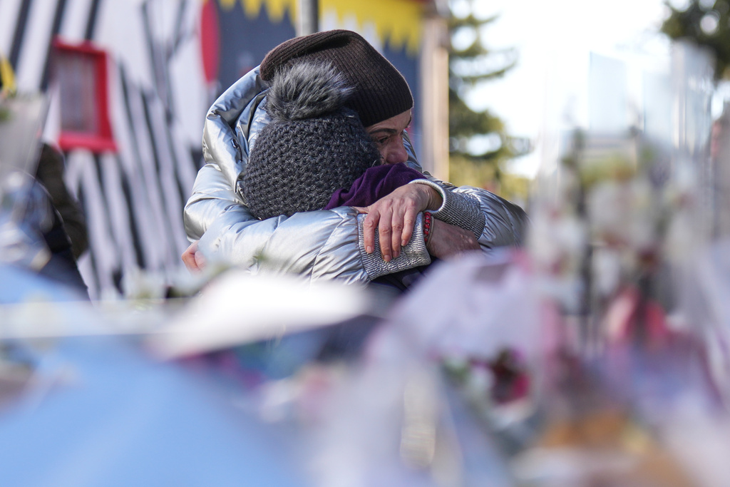 People mourn behind flowers and letters near the sealed off Le Constellation bar, where a devastating fire left dead and injured during the New Year's celebrations in Crans-Montana, Swiss Alps, Switzerland, Friday, Jan. 2, 2026. (AP Photo/ Antonio Calanni)