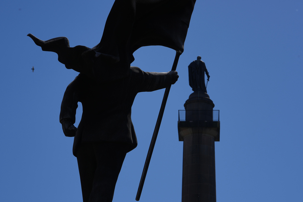 A statue of a man holding a flag which covers his face, left, and signed 'Banksy, has appeared in Waterloo Place in London, Thursday, April 30, 2026. (AP Photo/Kin Cheung)