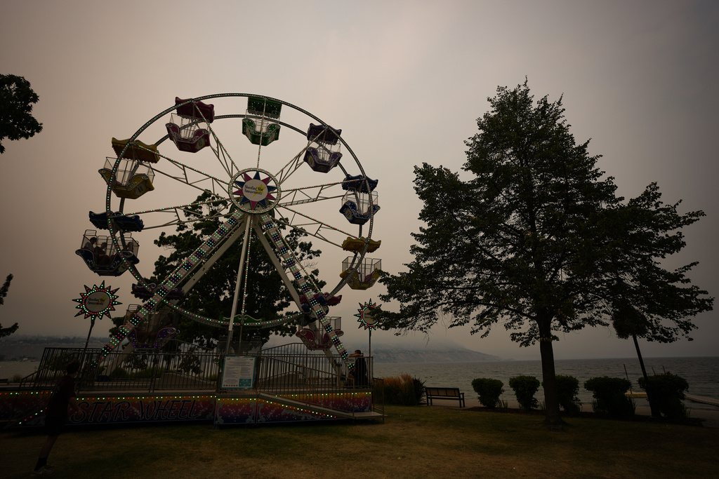 People ride a ferris wheel as smoke from the Bald Range wildfire envelops Okanagan Lake, in Penticton, British Columbia, on Sunday, Aug. 9, 2026. (Darryl Dyck/The Canadian Press via AP)