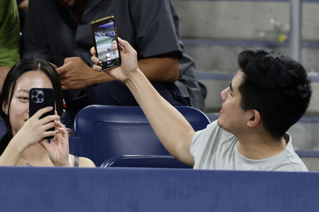 A fan takes a selfie as Elena Rybakina, of Kazakhstan, serves to Jessica Bouzas Maneiro, of Spain, during the second round of the U.S. Open tennis championships, Thursday, Sept. 3, 2026, in New York. (AP Photo/Adam Hunger)