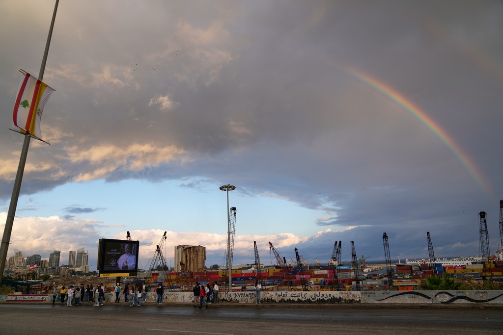 A rainbow rises behind the port and a billboard featuring Pope Leo XIV in Beirut, Lebanon, Tuesday, Dec. 2, 2025. (AP Photo/Hassan Ammar)