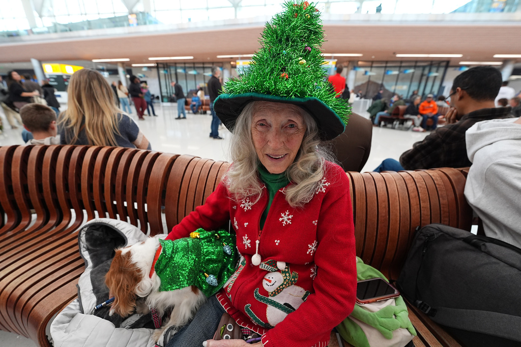 Linda Zimmerman of Bailey, Colo., wears holiday garb as she waits in the main terminal for the arrival of her daughter and granddaughters on a delayed flight from Minnesota with her 4-year-old Cavalier King Charles spaniel named Petunia in Denver International Airport Friday, Dec. 19, 2025, in Denver. (AP Photo/David Zalubowski)