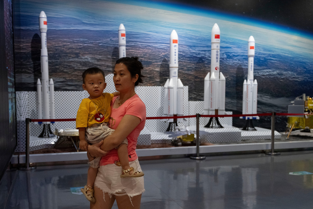 A woman carries a child as she walks past models of space rockets displayed in Haikou in southern China's Hainan province on Sunday, Aug. 23, 2026. (AP Photo/Ng Han Guan)
