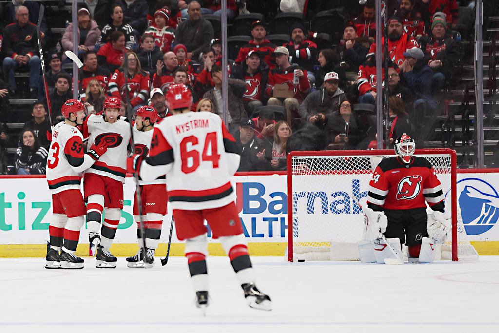 New Jersey Devils goaltender Jake Allen (34) looks on while Carolina Hurricanes left wing Taylor Hall, second from left, celebrates after his goal with teammates in the second period of an NHL hockey game, Sunday, Jan. 4, 2026, in Newark, N.J. (AP Photo/Heather Khalifa)
