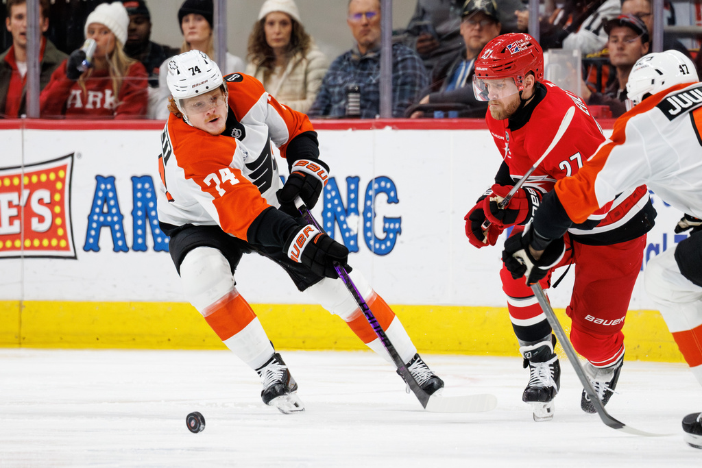 Philadelphia Flyers' Owen Tippett (74) sends the puck down the ice ahead of Carolina Hurricanes' Nikolaj Ehlers, center, during the second period of an NHL hockey game in Raleigh, N.C., Sunday, Dec. 14, 2025. (AP Photo/Ben McKeown)