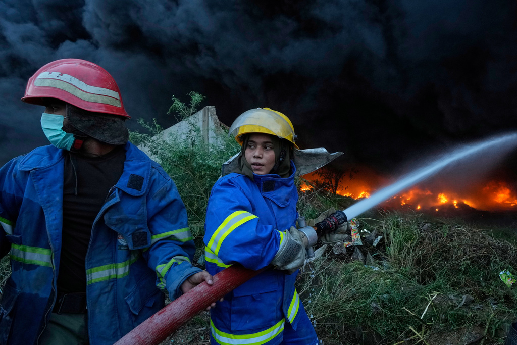 Female firefighter Syeda Masooma Zaidi, right, with her team member spray water to extinguish on a fire broke out in a storage facility packed vehicles tires, outskirts of Karachi, Pakistan, Thursday, Oct. 30, 2025. (AP Photo/Fareed Khan)