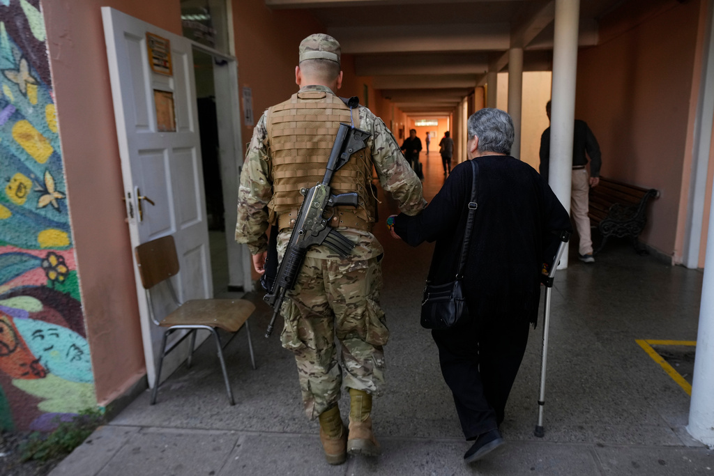A soldier walks with a voter inside a polling station during general elections in Santiago, Chile, Sunday, Nov. 16, 2025. (AP Photo/Esteban Felix)