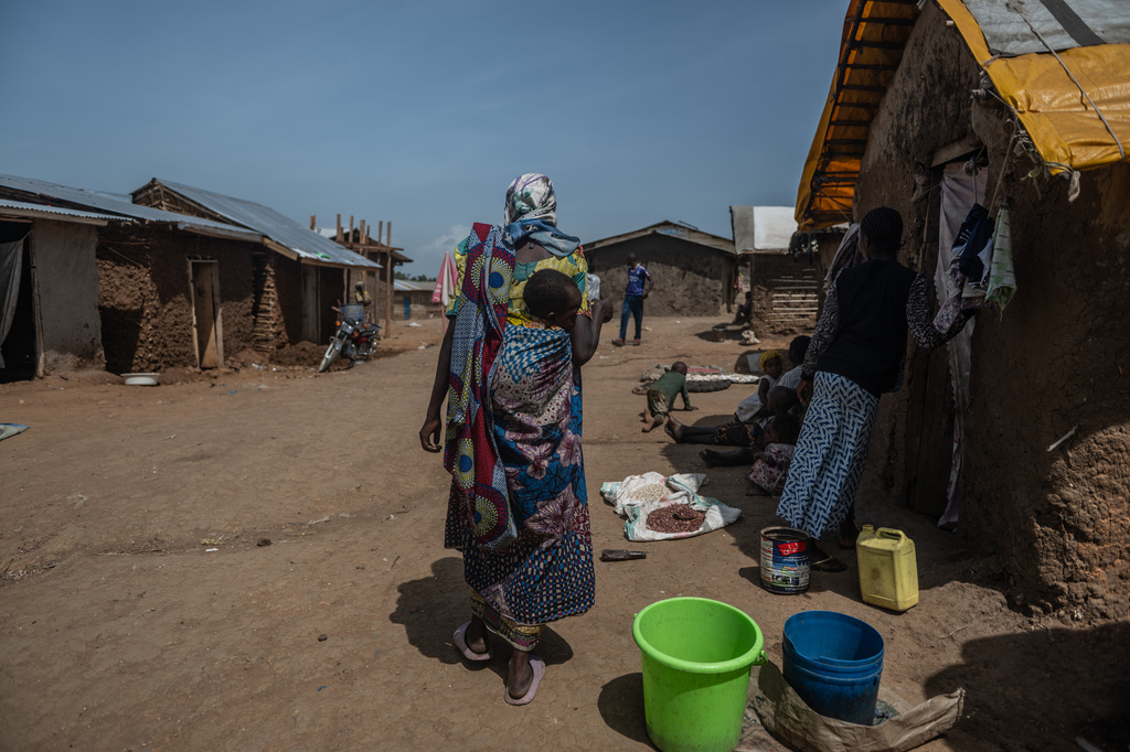 A woman carrying a child walks through the camp on the property of the city's ISP (Institut Supérieur Pédagogique), where internally displaced people reside in Bunia, Congo, Tuesday, May 26, 2026. (AP Photo/Moses Sawasawa)