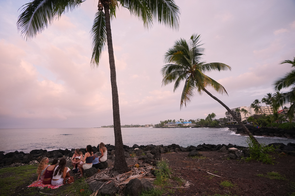 Members of Youth With A Mission read under a palm tree as Hurricane Nolo sits nearby Friday, Sept. 25, 2026, in Kona, Hawaii. (AP Photo/Gregory Bull)