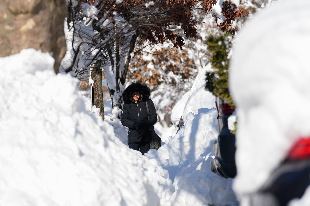 A woman navigates around piles of shoveled snow as she makes her way down a sidewalk, Tuesday, Feb. 24, 2026, in Weekhawken, N.J. (AP Photo/Seth Wenig)