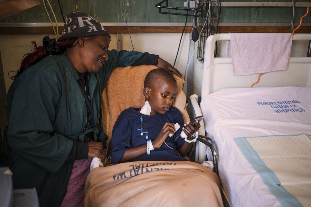 Violet Petro watches her 9 year-old son Ethan Goronga playing games on a mobile phone as he recovers from an open-heart surgery at Parirenyatwa Hospital, Harare, Zimbabwe, Thursday, July 17, 2025. (AP Photo/Aaron Ufumeli)
