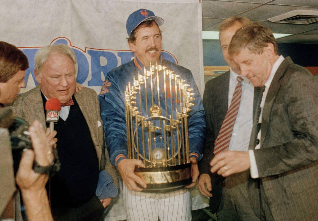 FILE - New York Mets Manager Davey Johnson, center, holds baseball's World Series trophy on the podium after the Mets defeated the Boston Red Sox in Game 7, at Shea Stadium in New York, Oct. 27, 1986. Mets General Manager Frank Cashen, left, Baseball Commissioner Peter Ueberroth, partially hidden, and Mets President Fred Wilpon, right, join the celebration in the locker room the clubhouse. (AP Photo/Ray Stubblebine, File)