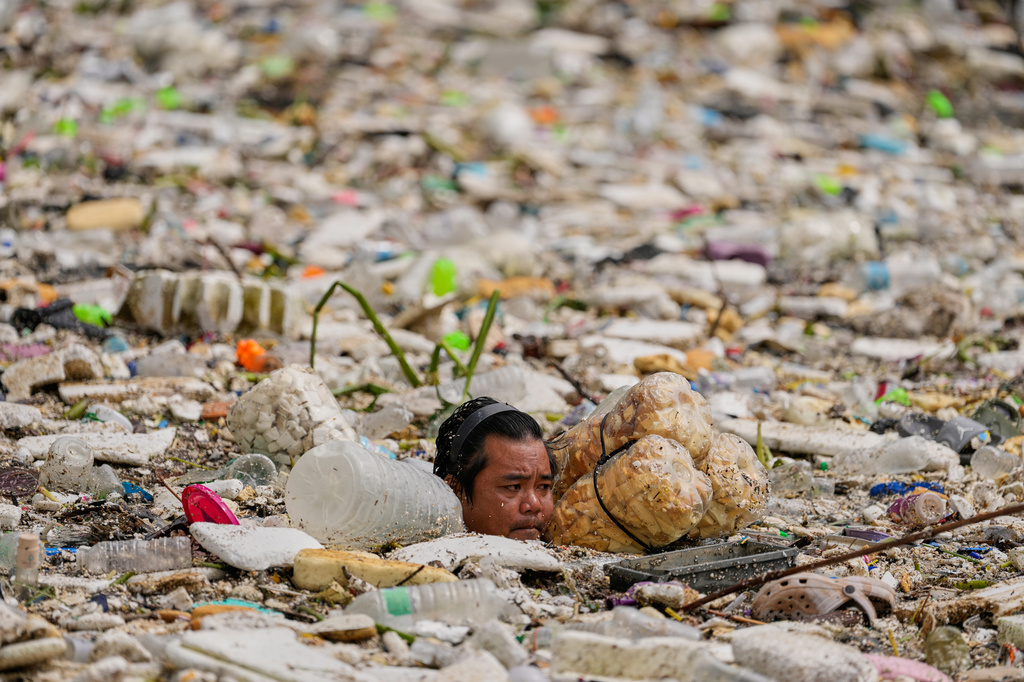 A worker uses improvised floats while trying to clear a sea of garbage and debris brought by intense monsoon rains at the Redemptorist Water Channel in Paranaque city, Metro Manila, Philippines on Tuesday, Aug. 11, 2026. (AP Photo/Aaron Favila)