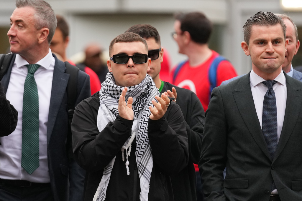 Liam Óg Ó hAnnaidh, aka Mo Chara, centre, a member of the Irish language band Kneecap, applauds as he leaves Woolwich Crown Court in London, Friday, Sept. 26, 2025, after Chief Magistrate, Senior District Judge Paul Goldspring, dismissed a terrorism offence relating to displaying a flag in support of Hezbollah during a performance with the band in November 2024, on a technical error. (AP Photo/Joanna Chan)