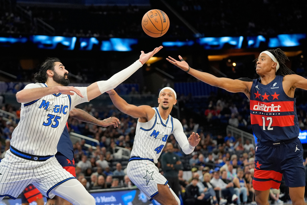 Orlando Magic center Goga Bitadze (35), guard Jalen Suggs (4) and Washington Wizards guard Tre Johnson (12) go after a rebound during the first half of an NBA basketball game, Tuesday, March 3, 2026, in Orlando, Fla. (AP Photo/John Raoux)