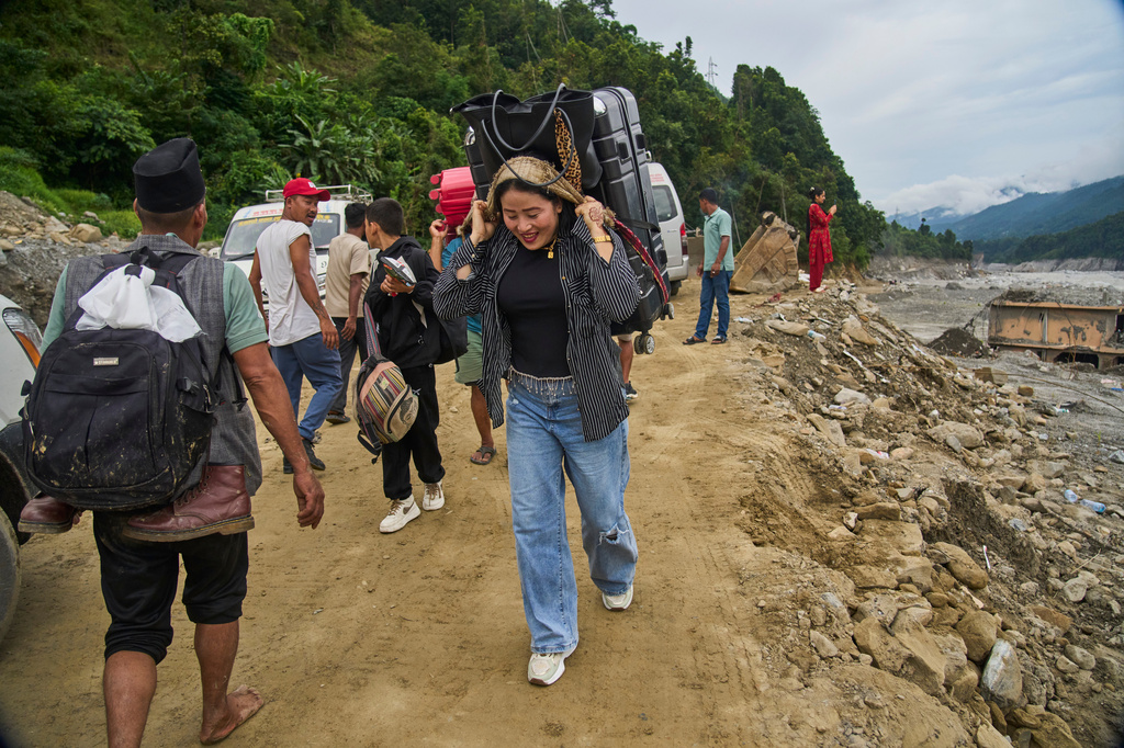 People carry their belongings as they walk toward their villages after flash floods damaged roads in Nepal's Nuwakot district, Wednesday, Sept. 23, 2026. (AP Photo/Niranjan Shrestha)