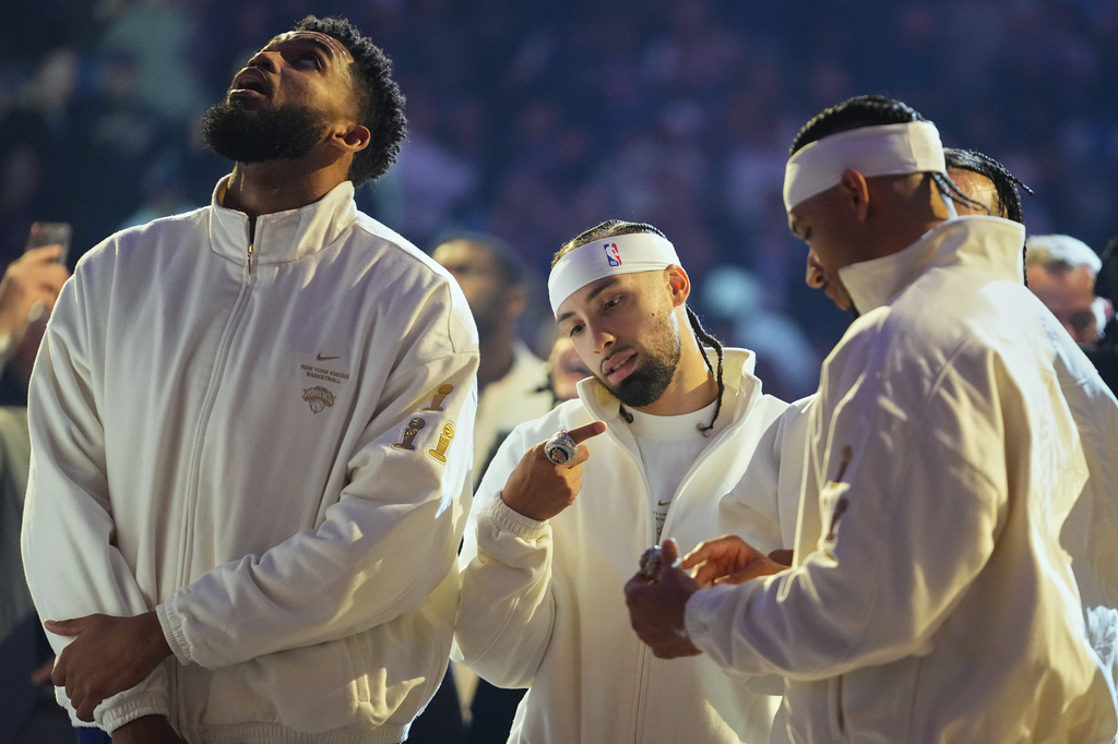 New York Knicks guard Jose Alvarado, center, looks at his 2025-26 World Champions ring alongside teammates center Karl-Anthony Towns, left, and guard Josh Hart before an NBA basketball game against the Philadelphia 76ers Tuesday, Oct. 20, 2026, in New York. (AP Photo/Frank Franklin II)
